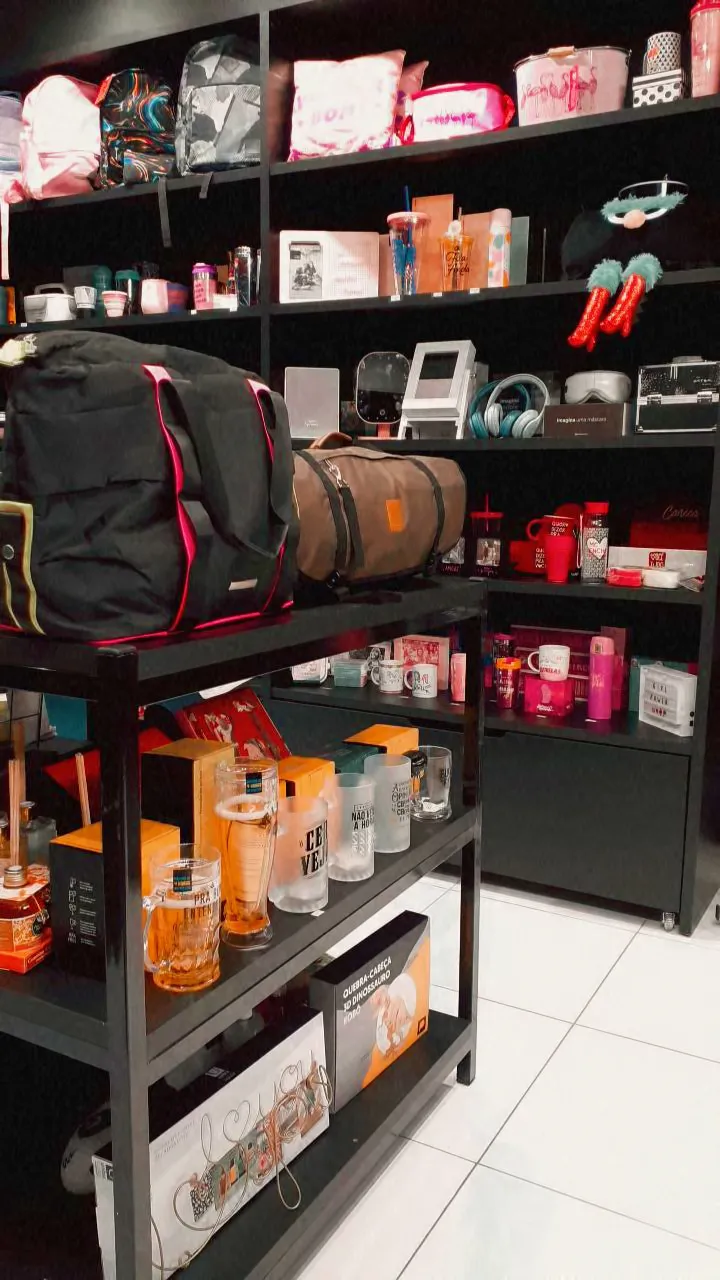 Prateleiras com bolsas, canecas, copos e presentes criativos da Mimos e Presentes